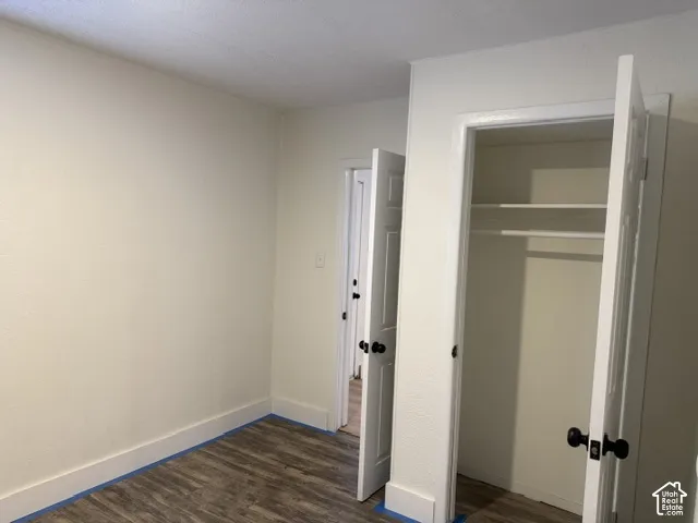 Interior room featuring wood-finish flooring, white walls, and a closet with built-in shelving