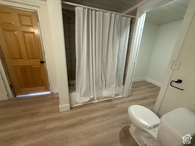 Bathroom featuring wood-finish flooring, a tub-shower combination with tiled surround, a solid wood six-panel door, and a wall-mounted matte black towel ring
