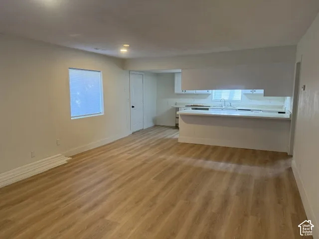 Open-concept interior featuring light-tone wood-finish flooring, white cabinetry, a kitchen peninsula with a countertop, and recessed lighting