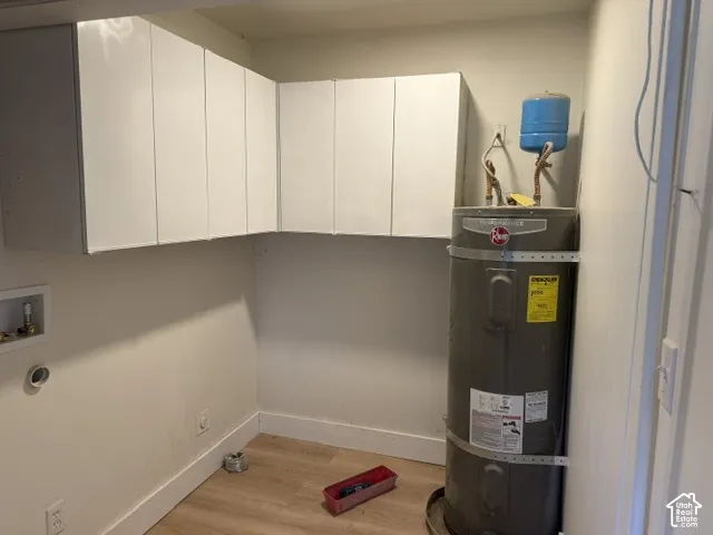 White wall-mounted cabinetry, wood-finish flooring, and a water heater with expansion tank