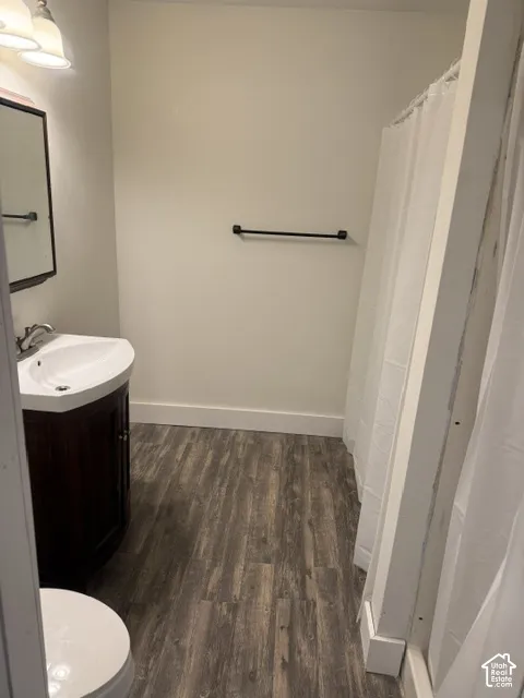 Bathroom featuring a dark wood-finish vanity, integrated sink with chrome faucet, wood-finish flooring, and a matte black towel bar