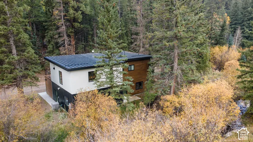 Contemporary multi-level exterior featuring a combination of horizontal wood-finish siding, white stucco, and vertical black metal paneling, topped with a flat metal roof