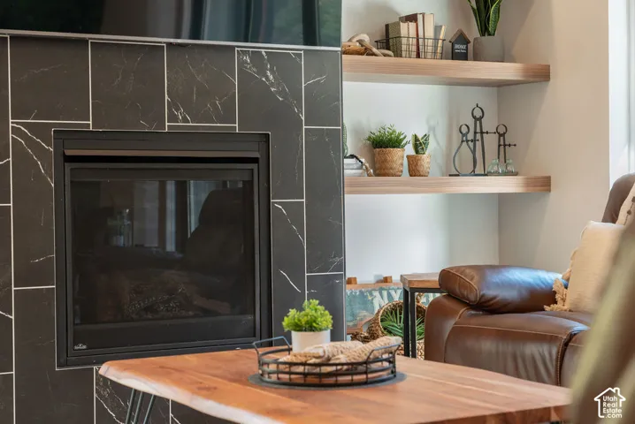 Fireplace featuring black tile surround with linear veining and wood-finish floating shelves