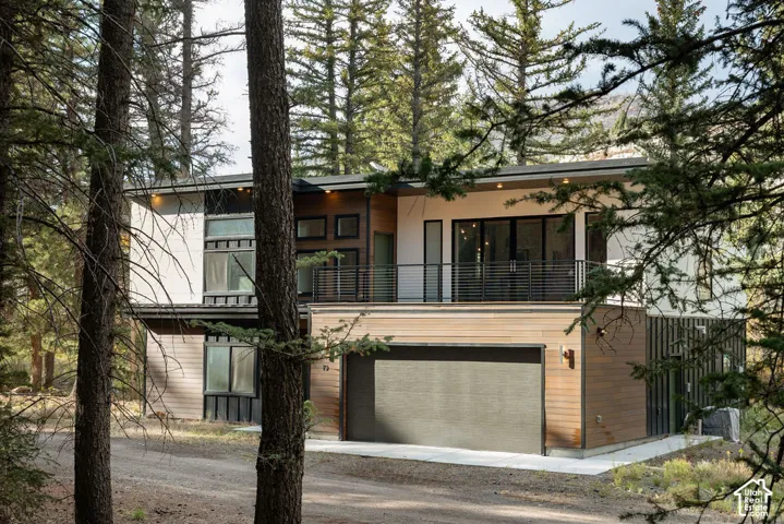 Contemporary multi-level exterior featuring wood-tone paneling, metal siding, a second-story balcony with horizontal cable railing, and an attached garage