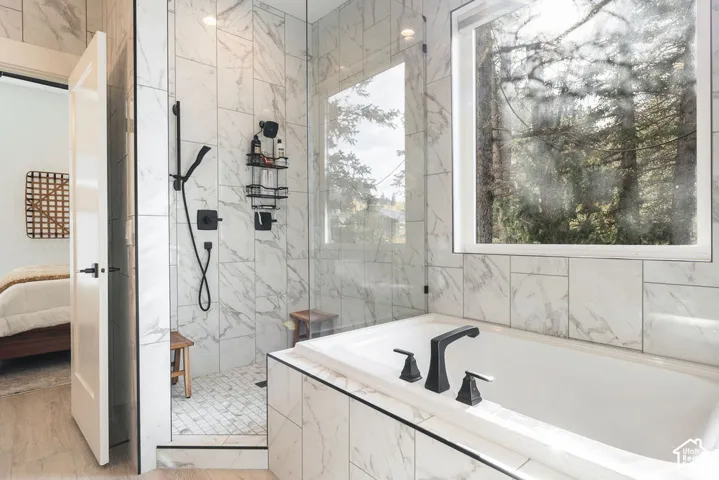 Soaking tub with a wide-format window and matte black faucet, paired with a walk-in shower featuring large-format veined tile, a glass enclosure, and a handheld showerhead