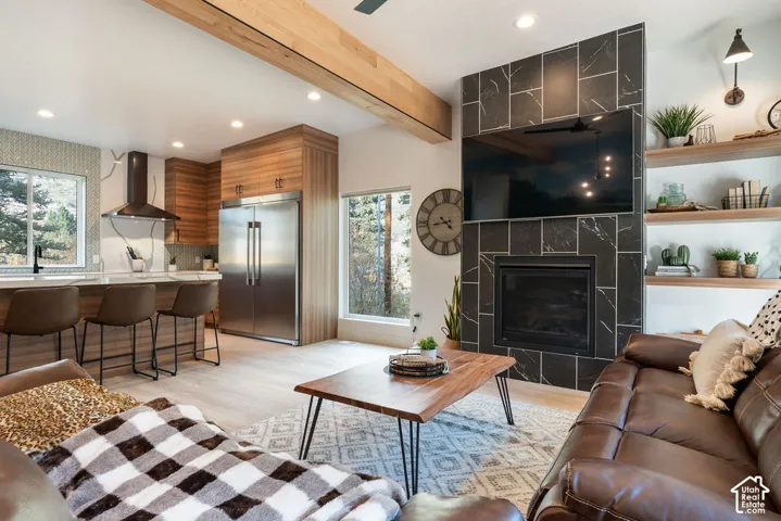 Open concept living area featuring a floor-to-ceiling tiled fireplace, exposed structural timber beam, built-in wall shelving, custom cabinetry, and recessed lighting