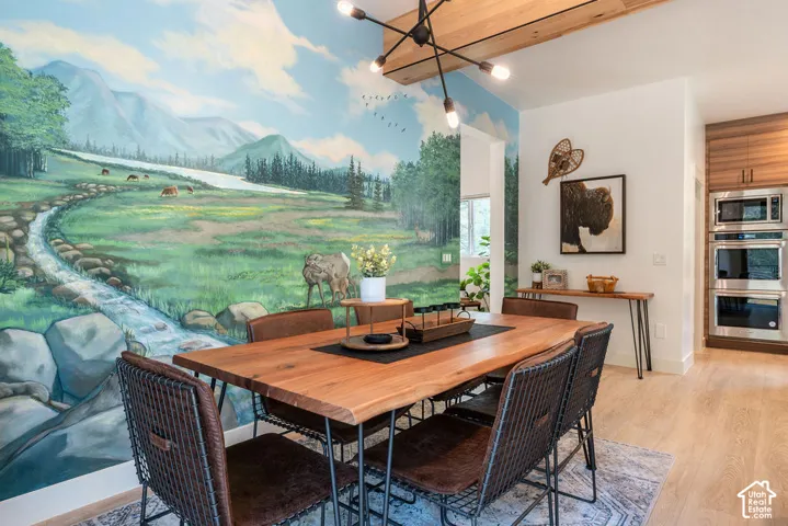Custom landscape mural, wood-finish flooring, exposed wood ceiling beam, modern multi-arm light fixture, and built-in stainless steel double wall ovens