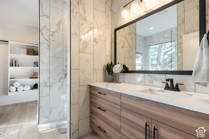 Bathroom featuring a wood-finish vanity with a quartz countertop, rectangular under-mount sink, matte black faucet, and full-height stone-patterned wall tile