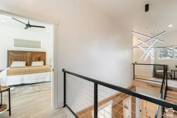 Modern geometric linear chandelier, sliding barn-style door, wood-finish flooring, and industrial-style metal railing with horizontal cable infill