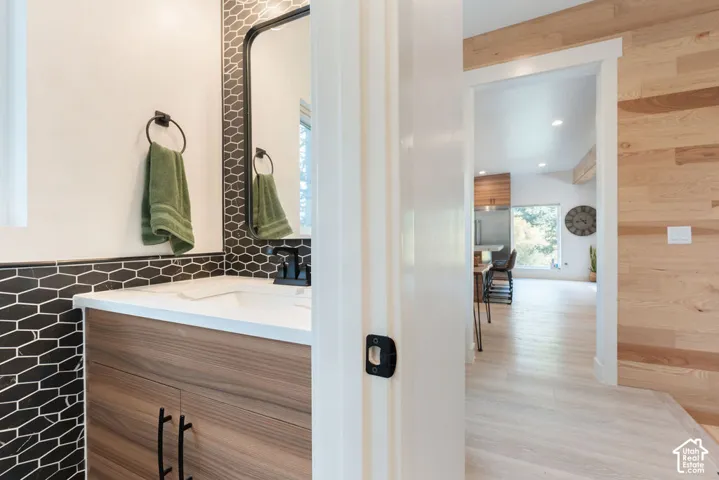 Bathroom featuring a wood-finish vanity with a white countertop, black hexagonal tile backsplash, rounded rectangular mirror, and matte black hardware, accented by natural wood-plank wall paneling