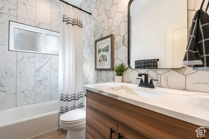 Bathroom featuring a wood-finish vanity with a white countertop, matte black faucet, geometric wall tile, and a rectangular mirror with a black frame