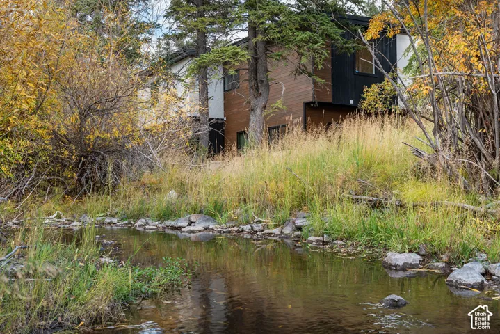 Modern exterior featuring mixed-material cladding, natural landscape setting with mature trees, and a perennial creek