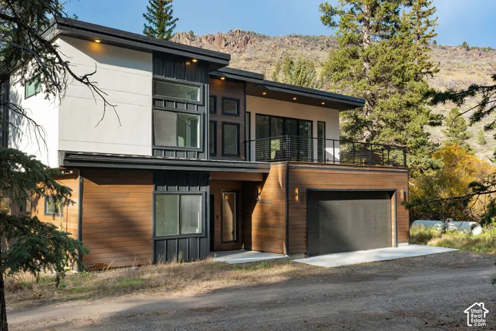 Contemporary exterior featuring mixed-material siding, large horizontal wood-finish cladding, an attached garage, and an upper-level balcony with metal railing