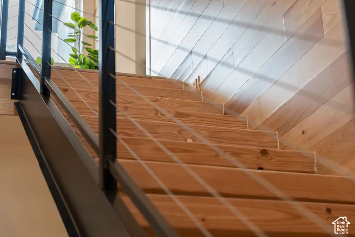 Staircase featuring natural wood treads, a matte black steel stringer, and a horizontal cable railing system with wood-plank wall paneling
