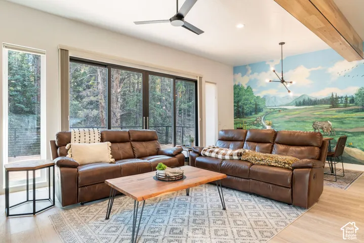 Living area featuring large sliding glass doors, a decorative wall mural, a natural wood ceiling beam, modern matte black ceiling fan, and recessed lighting