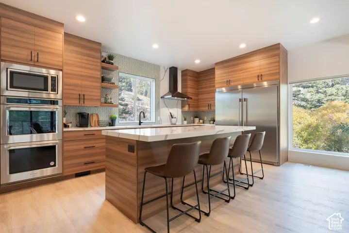 Kitchen featuring horizontal wood-grain cabinetry, waterfall-edge quartz countertops, stainless steel appliances, patterned tile backsplash, and recessed lighting