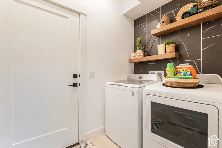 Laundry space featuring dark vertical-tile wall detailing, natural wood floating shelves, and a solid-core door with matte black hardware