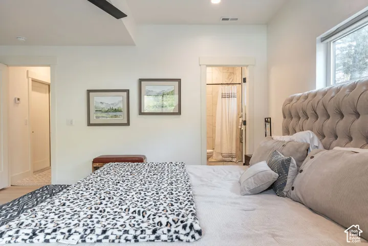 Neutral-toned bedroom featuring recessed ceiling lighting, a wide-cased doorway, light-toned wood-finish flooring, and a second cased opening providing entry to a tiled shower area