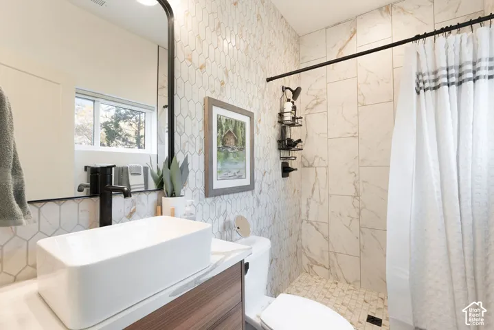 Bathroom featuring a wood-finish vanity, rectangular vessel sink, matte black faucet, full-height hexagonal wall tile, and vertical shower wall tile