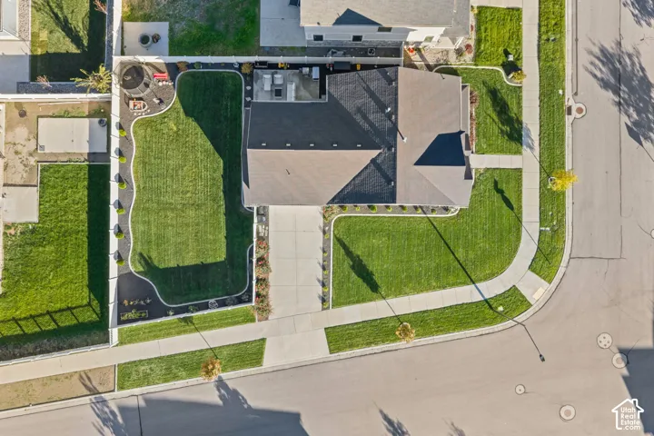 Aerial view of a corner lot featuring a concrete driveway, a fully fenced backyard with a manicured lawn, and a paved patio
