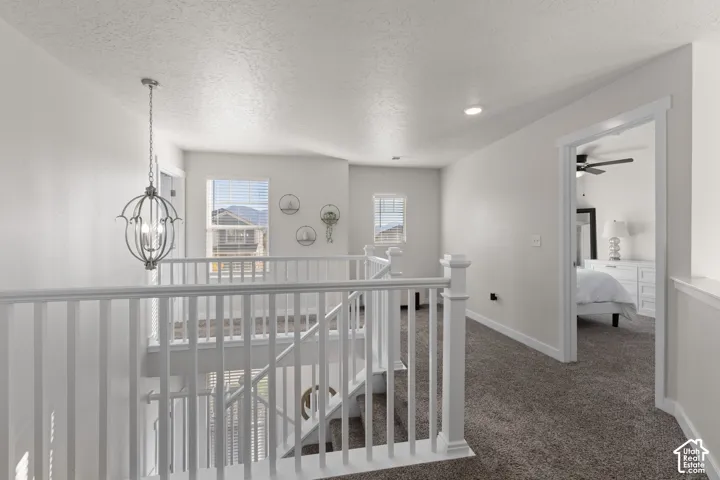 Neutral interior featuring a white-painted wooden balustrade, orb-style pendant lighting, recessed ceiling lighting, and wall-to-wall carpeting
