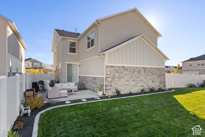 Exterior elevation featuring a combination of stone veneer and siding, concrete rear patio, fenced backyard, and manicured lawn