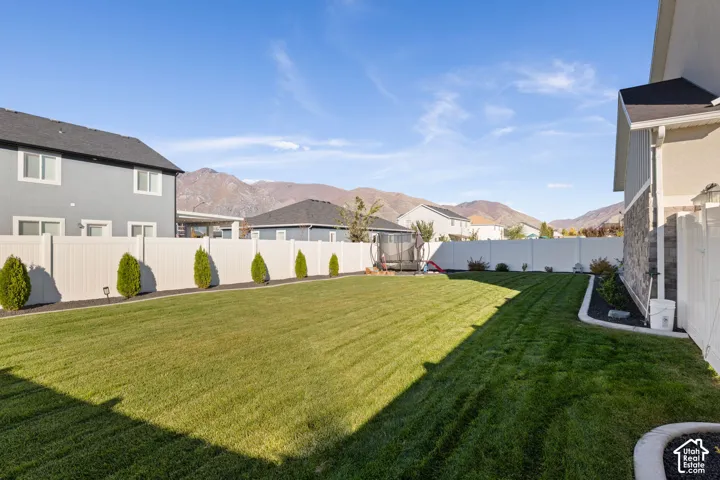 Backyard featuring a manicured lawn, white vinyl fencing, stone and siding exterior elements, and mountain scenery