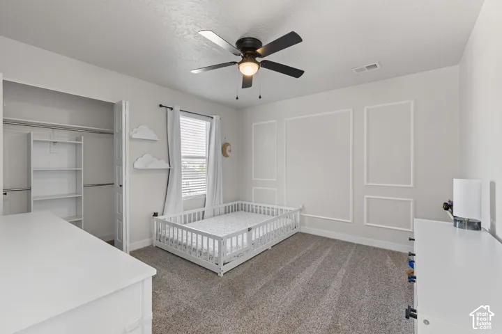Neutral-toned carpeting, wall molding accent panels, matte black ceiling fan with integrated light fixture, and walk-in closet with built-in shelving
