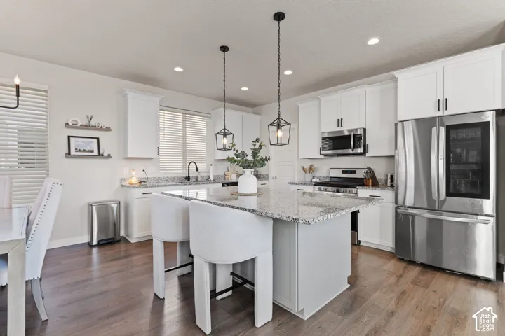 Kitchen featuring white shaker-style cabinetry, stone countertops, central island, stainless steel appliances, and wood-finish flooring