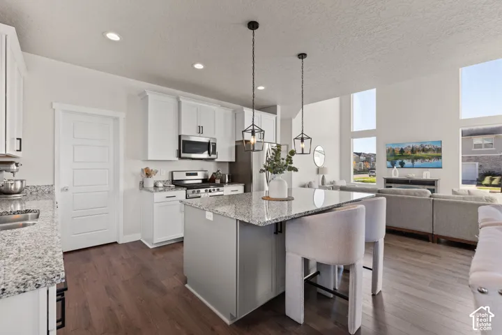Kitchen featuring white cabinetry, stone countertops, central island, wood-finish flooring, and vaulted ceilings with pendant lighting
