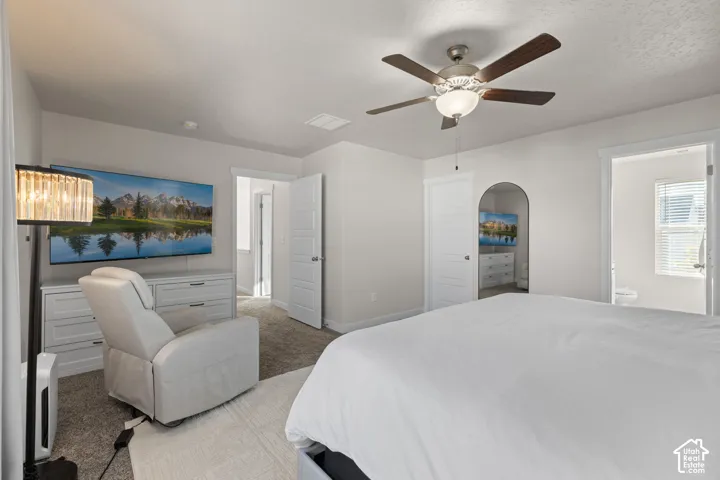 Neutral-toned interior featuring carpeted flooring, a ceiling fan with integrated lighting, and an arched doorway