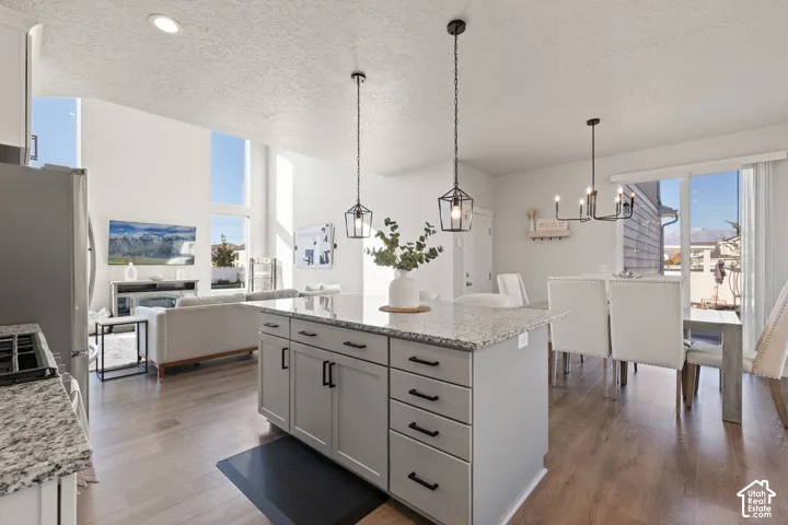 Kitchen featuring a central island with stone countertop, wood-finish flooring, two hanging pendant lights, and high ceilings with tall windows