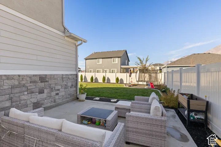 Rear concrete patio featuring stone veneer siding, white vinyl privacy fencing, manicured lawn, and mountain backdrop