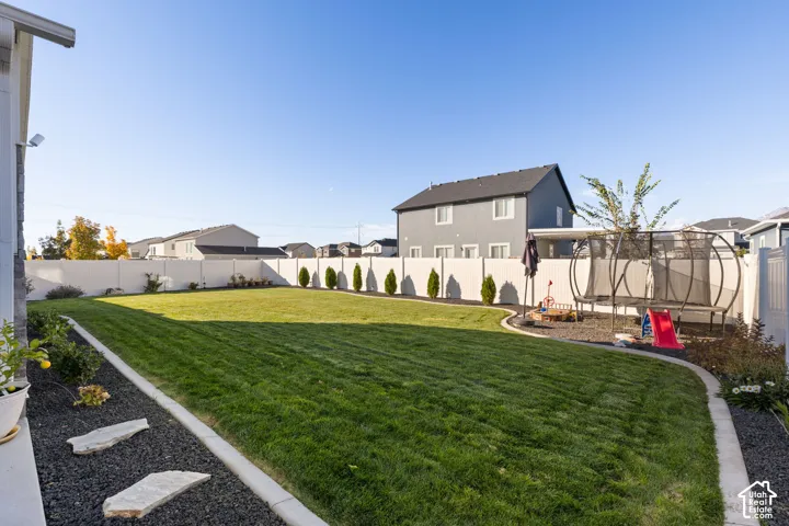 Backyard featuring a manicured lawn, white vinyl fencing, concrete curbing, and decorative rock landscaping