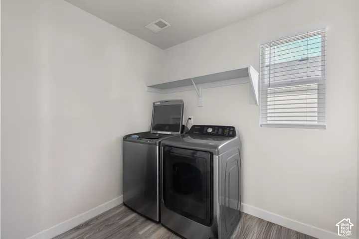 Laundry space featuring wood-finish flooring, a wall-mounted shelving unit, and a window with horizontal blinds