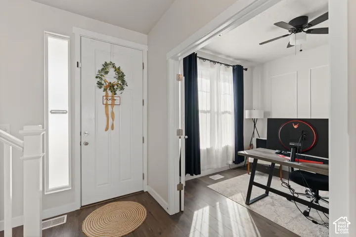 Entry featuring a white paneled front door with a vertical sidelight, wood-finish flooring, and a room entry defined by wide door casing, wall molding, and a ceiling-mounted fan