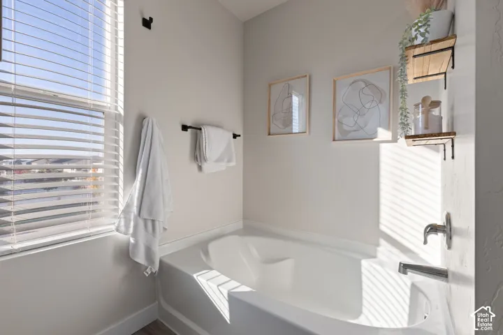 Deep soaking tub with a chrome faucet fixture, horizontal slatted window blinds, and matte black hardware