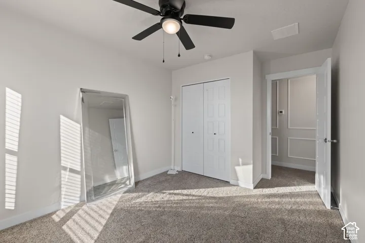 Neutral-toned interior featuring wall-to-wall carpeting, a ceiling fan with integrated lighting, and a dual-panel closet door
