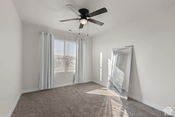 Neutral-toned carpeted flooring, window with integrated blinds, and five-blade ceiling fan with central light fixture