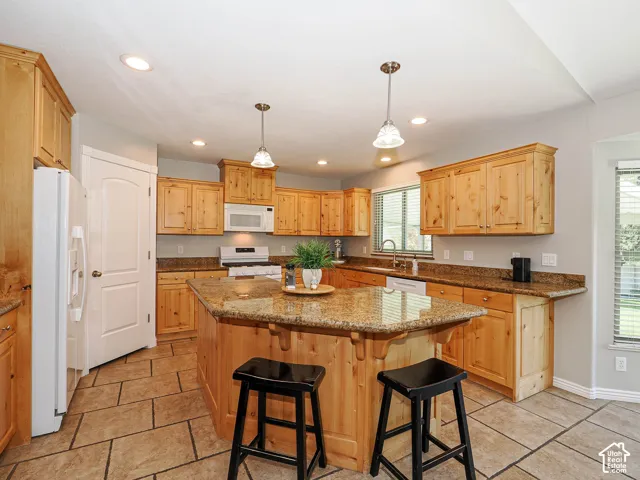 Kitchen featuring natural wood cabinetry, granite countertops, a center island with seating area, recessed lighting, and tile flooring
