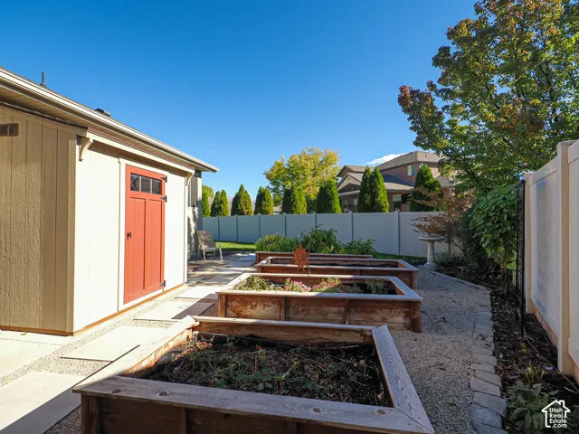 Featuring three raised cedar garden beds, crushed stone landscaping, a vinyl privacy fence, and a storage shed with a contrasting red door
