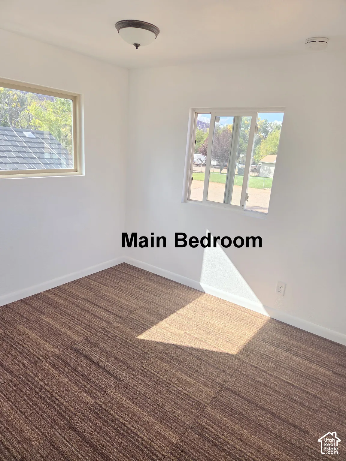 Room featuring neutral walls, wood-finish flooring, two sliding windows, and a flush-mount ceiling light fixture