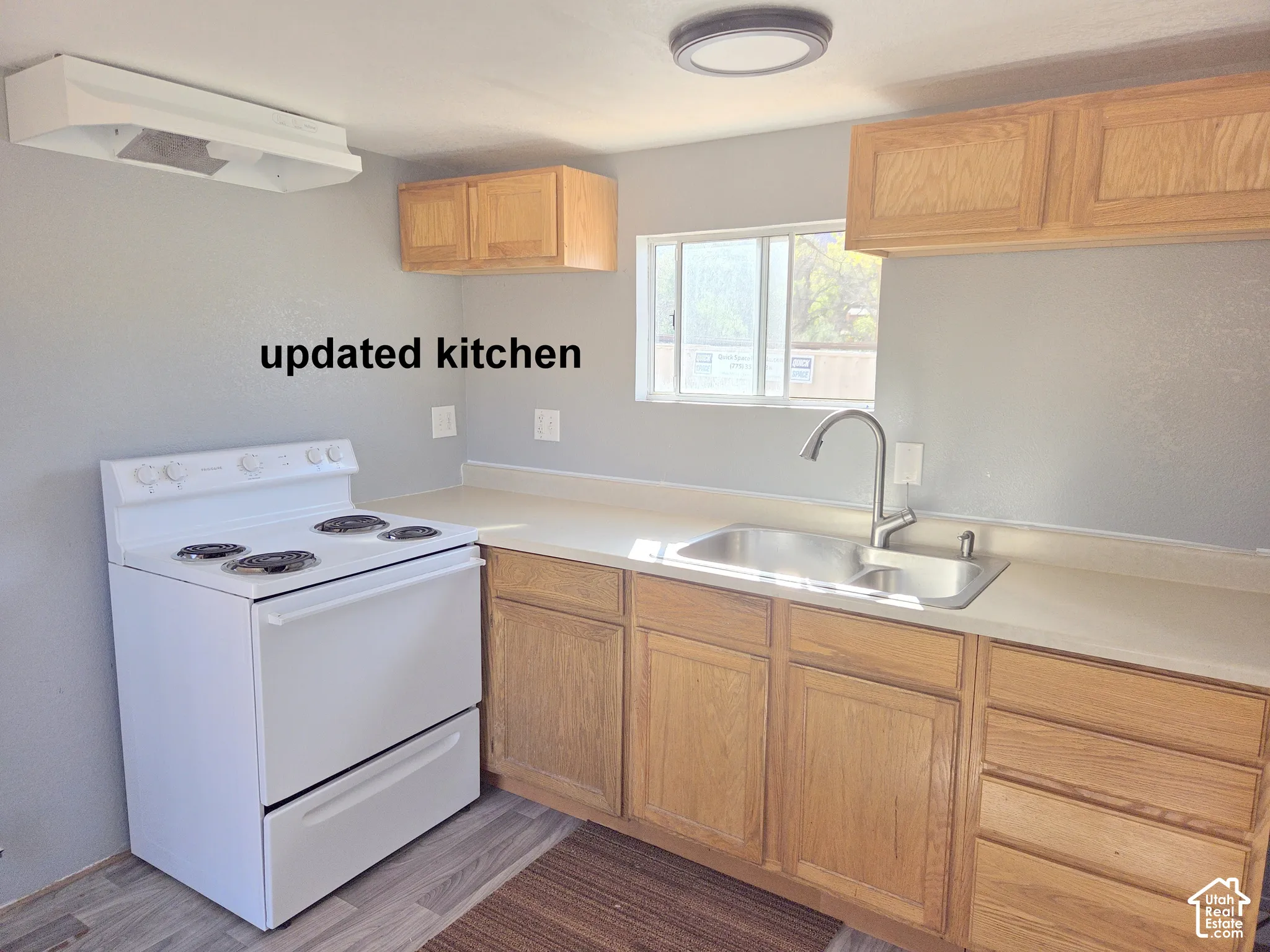 Kitchen featuring wood cabinetry, solid surface countertops, stainless steel dual-basin sink with gooseneck faucet, white electric range, and wood-finish flooring