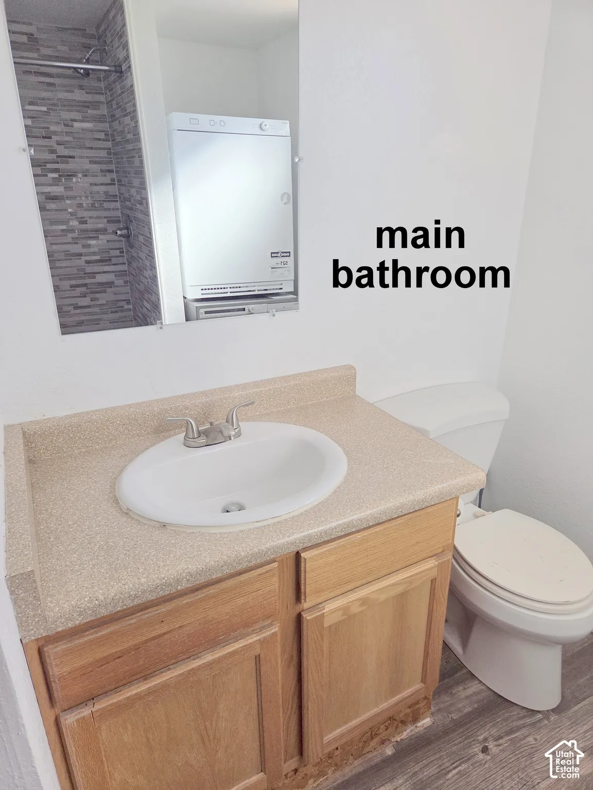 Bathroom vanity featuring a speckled countertop with an integrated oval basin, wooden cabinetry, two-handle metal faucet, and wood-finish flooring