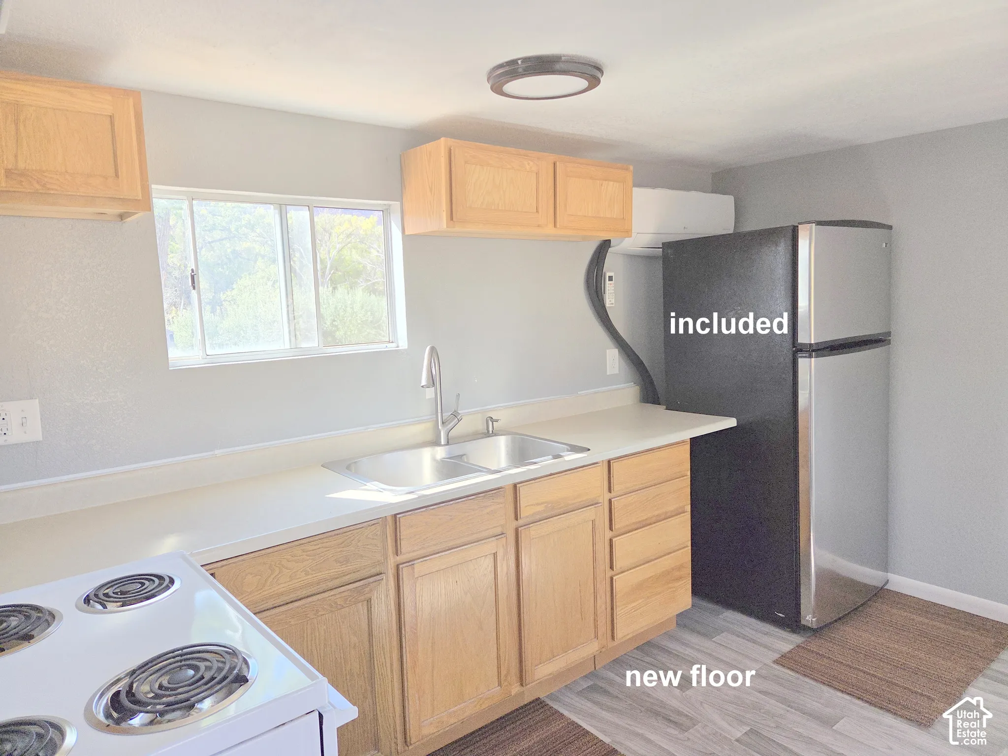 Kitchen area featuring natural wood cabinetry, solid-surface countertops, a dual-basin stainless steel sink with high-arc faucet, and wood-finish flooring