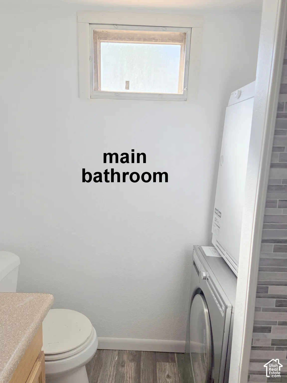 Bathroom featuring a stackable laundry unit, wood-finish flooring, a neutral-toned countertop, and a recessed window