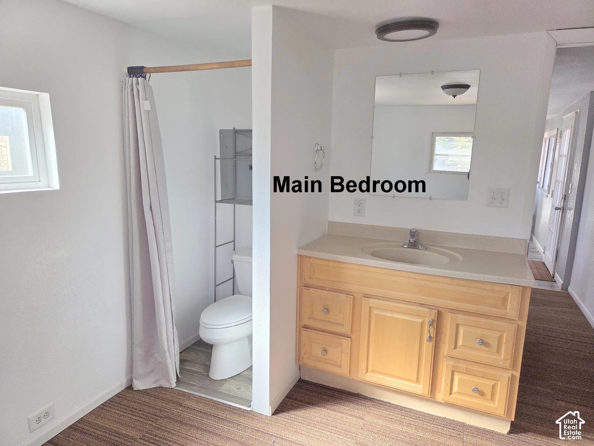 Vanity featuring light wood-finish cabinetry, integrated basin, and solid-surface countertop, accompanied by a wall-mounted mirror and commode