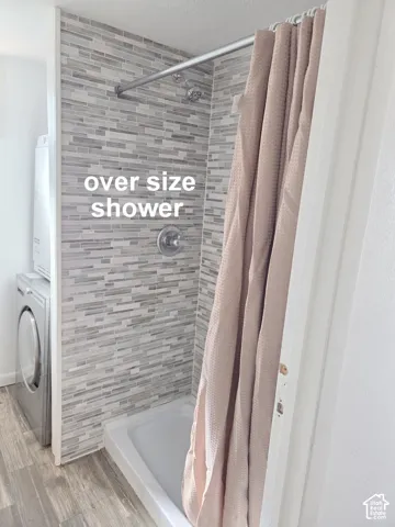 Shower enclosure featuring horizontal multi-tonal linear tile surround, integrated showerhead, chrome finish control valve, and wood-finish flooring
