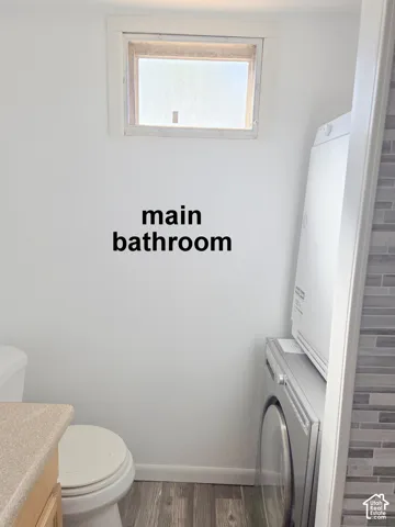 Bathroom featuring a stackable laundry unit, wood-finish flooring, a neutral-toned countertop, and a recessed window