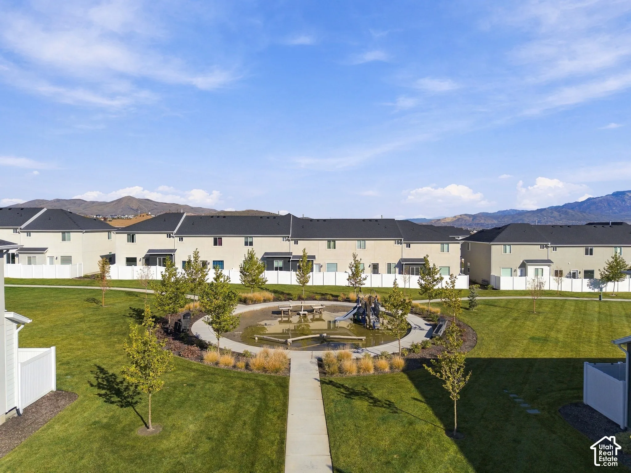 Common area featuring a central playground, manicured lawn, concrete walking paths, and mature landscaping set against a mountain backdrop